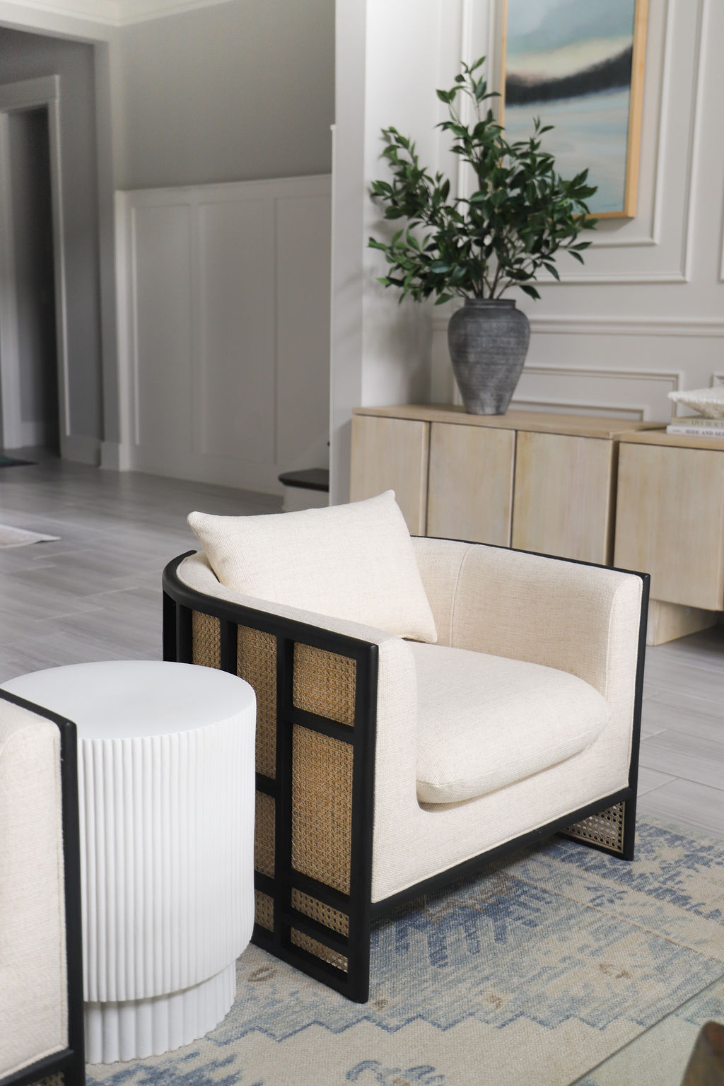 This chair has a woven back and dark wood with white beige cushions. The side table is fluted. Both fit into this modern coastal living room.