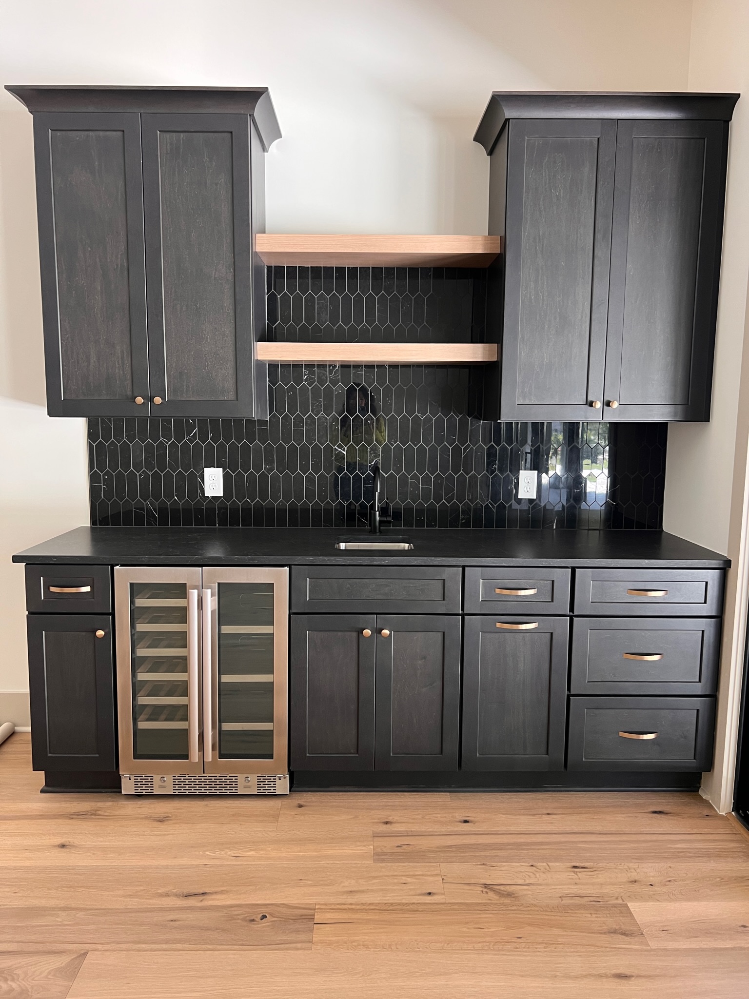 These beautiful dark tiles make the perfect backsplash for the wet bar. The wet bar features dark wood cabinets and lighter wood open shelving near the top.
