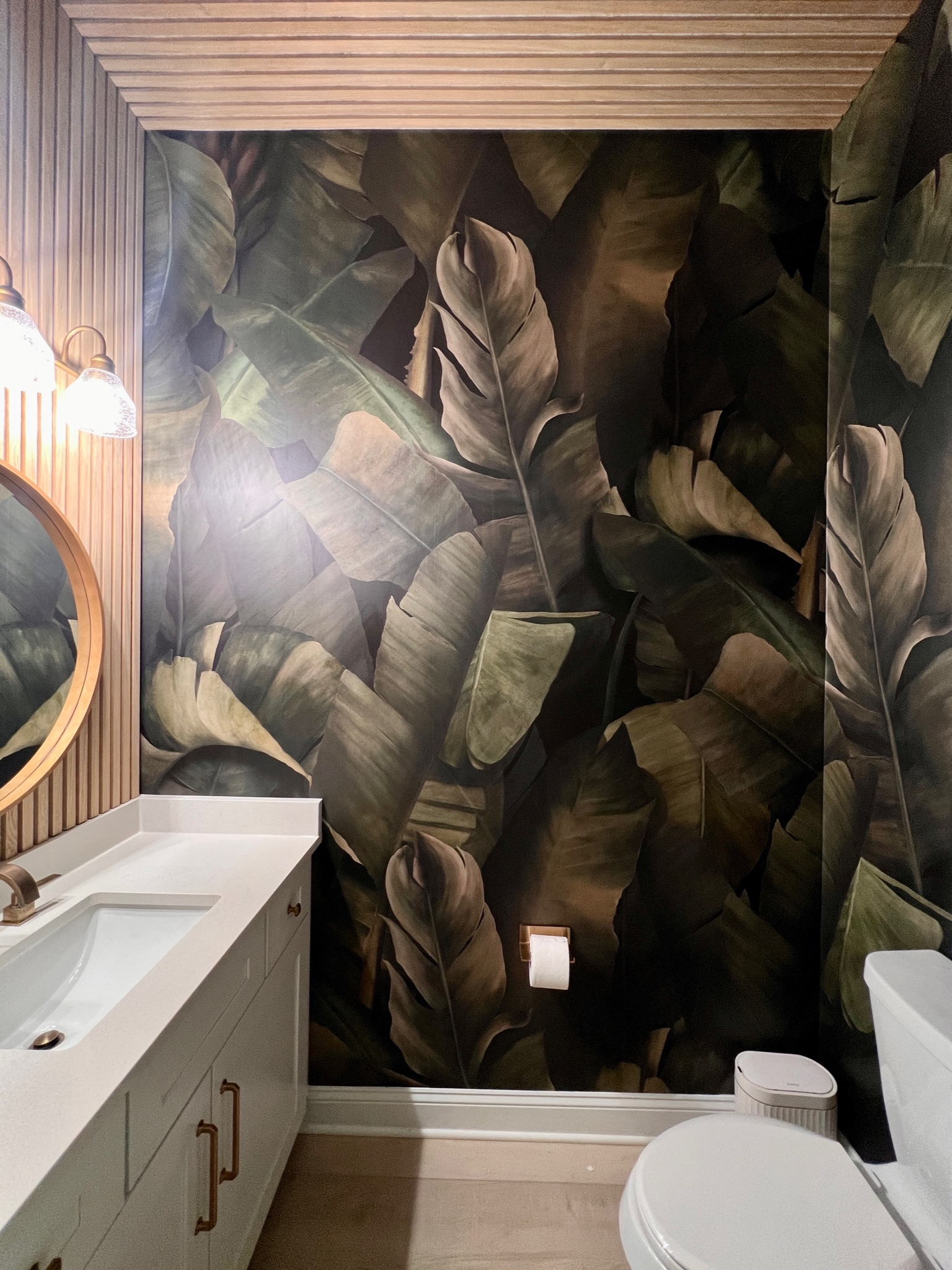 This powder room is accented with a dark tropical wallpaper and wood paneling wall treatment.