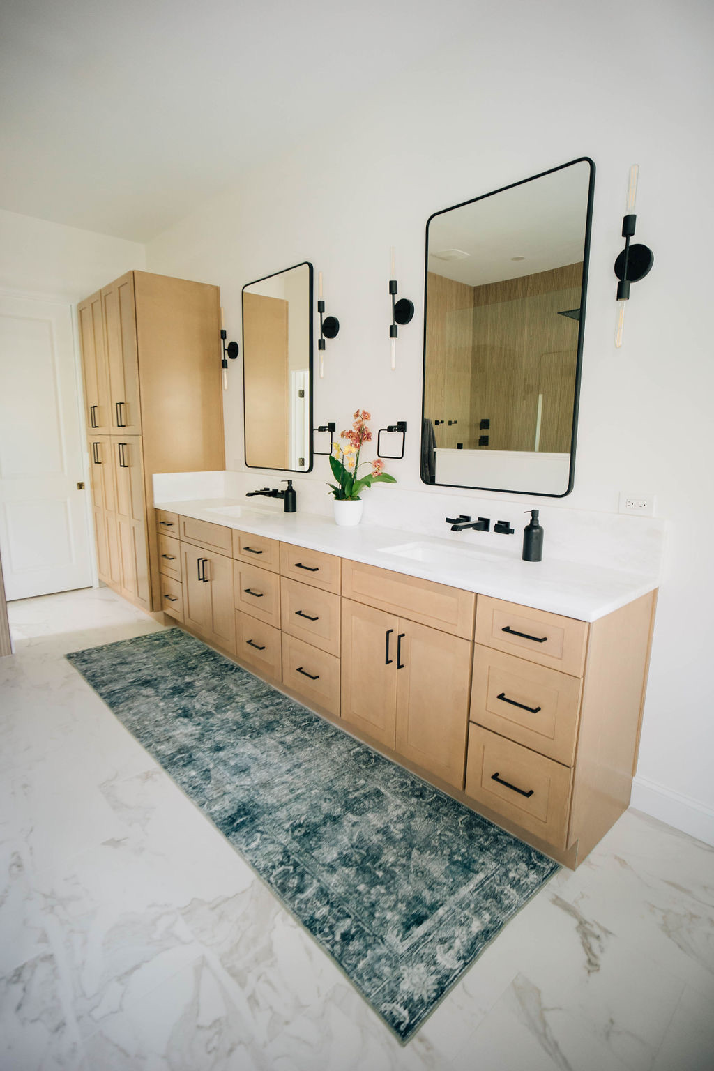 This gorgeous bathroom remodel features light-colored wood cabinets, marble flooring, and unique finishings in striking black metal.