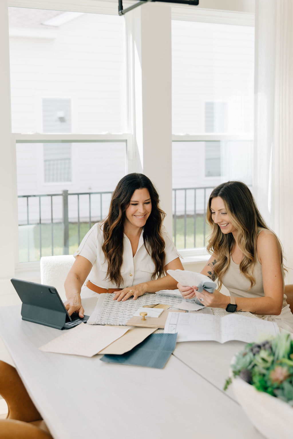 Two women engaged in discussion at a table, with a laptop and papers spread out before them.