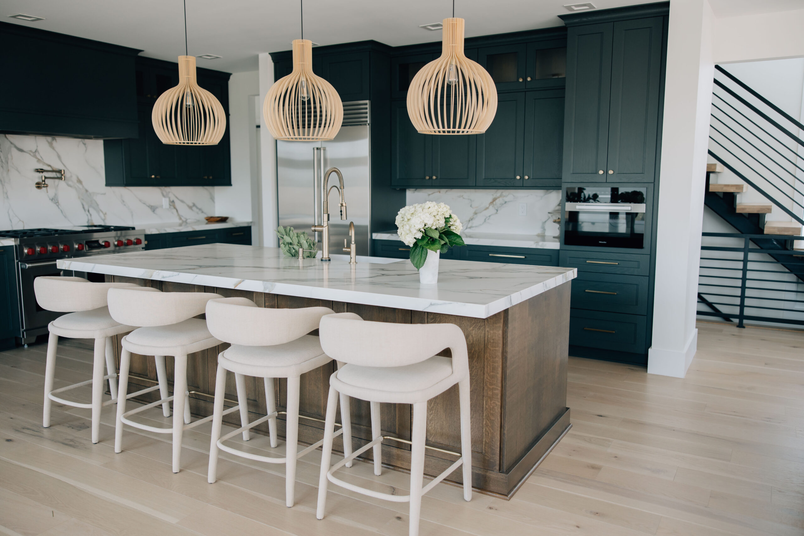 a kitchen with bold, dark cabinets, natural light fixtures, marble countertops, a warm wood island, and cream bar stools.
