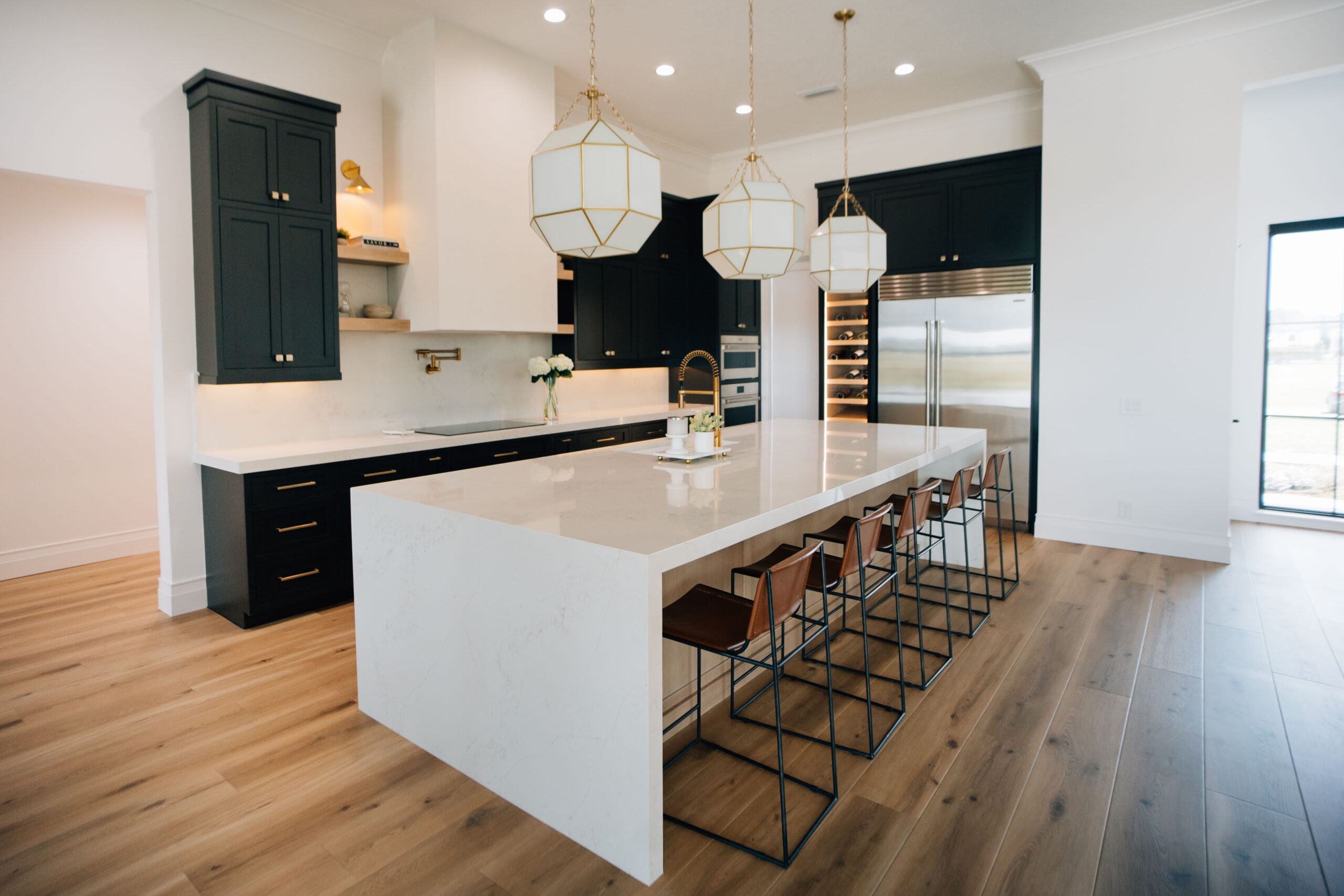 A Kitchen that Wows Welcome Home styling provides interior design services for kitchens. The Delaney kitchen showcases a waterfall quartz countertop island, dark cabinets, and modern light fixtures.