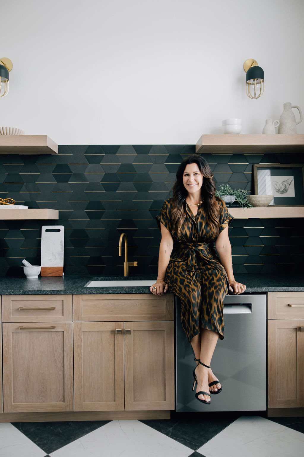 A full service interior designer seated in a modern butler’s pantry featuring geometric tile, natural wood cabinetry, and curated styling.