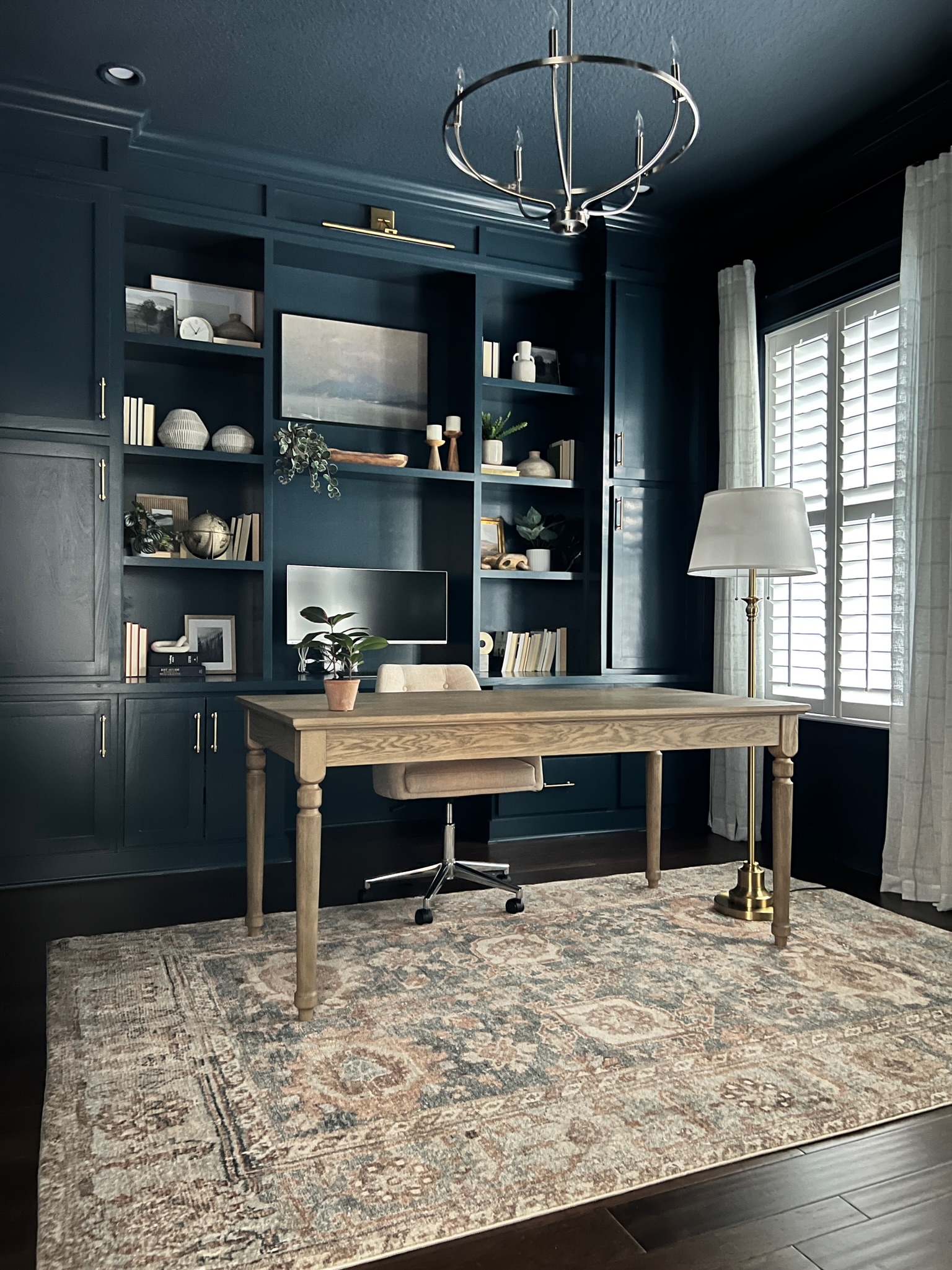 A rich and moody home office redesign featuring navy built-in shelving, curated decor, and a statement light fixture, designed by a Jacksonville full service interior designer.