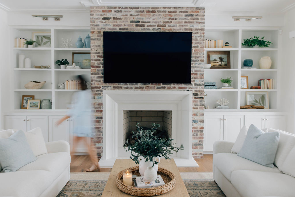 This living room, styled by Welcome Home Styling, features custom built-ins, an exposed brick fireplace, personalized decor, and a full service interior designer on the move.