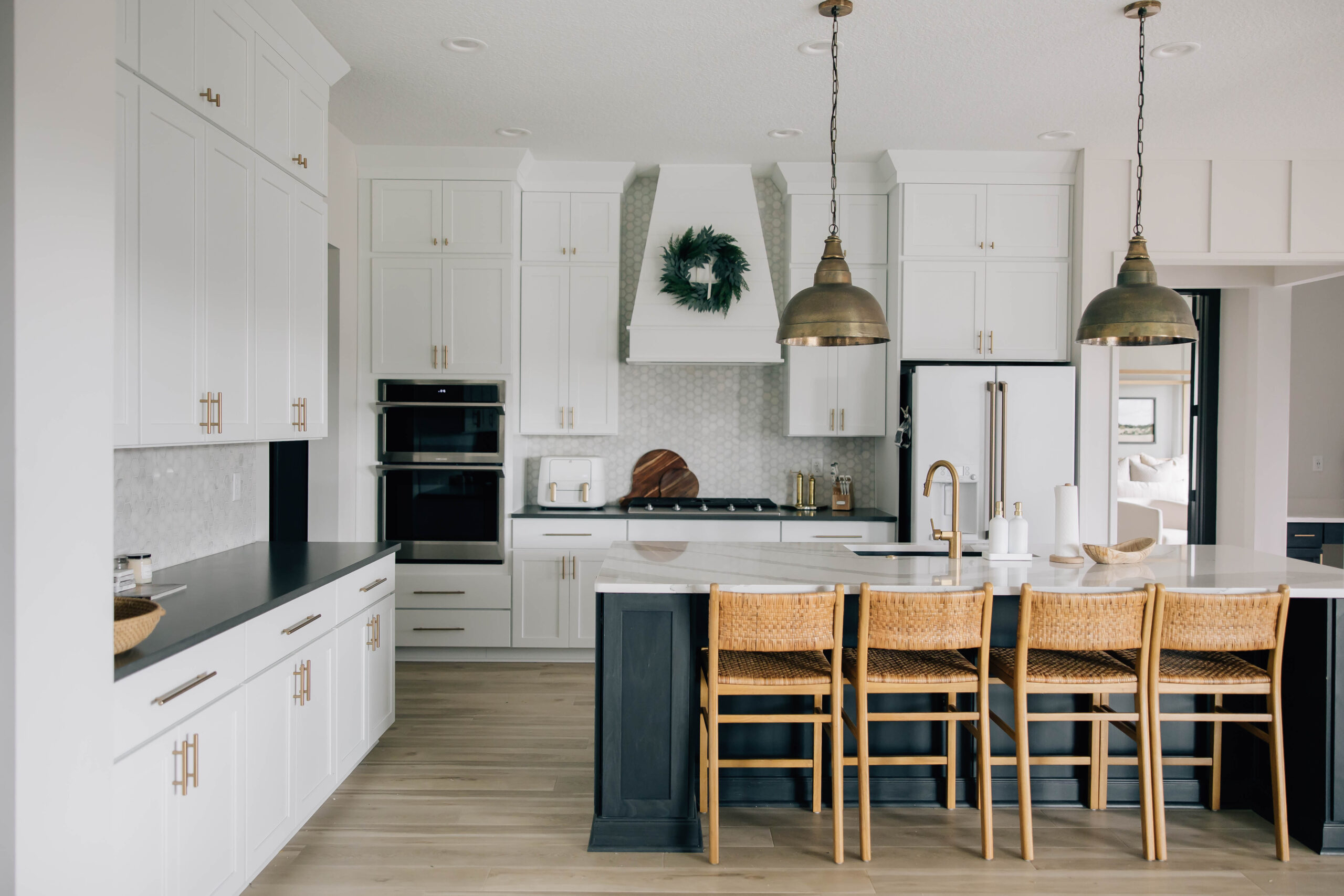Bright and elegant kitchen design featuring a white and brass color palette, large island with woven seating, and pendant lighting by a St. Johns County interior design firm