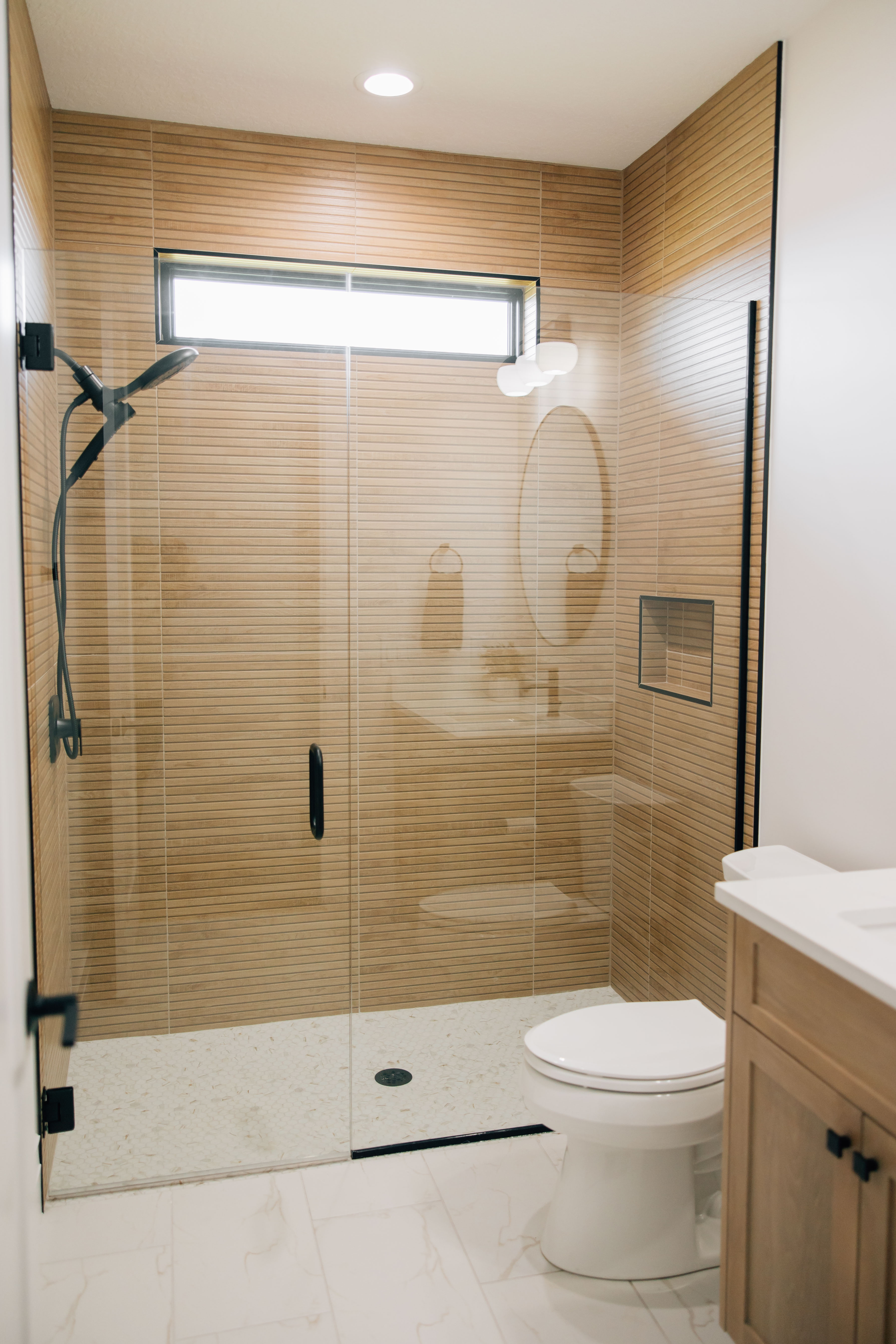 Modern bathroom with wood-look tile, glass shower enclosure, and built-in niche.