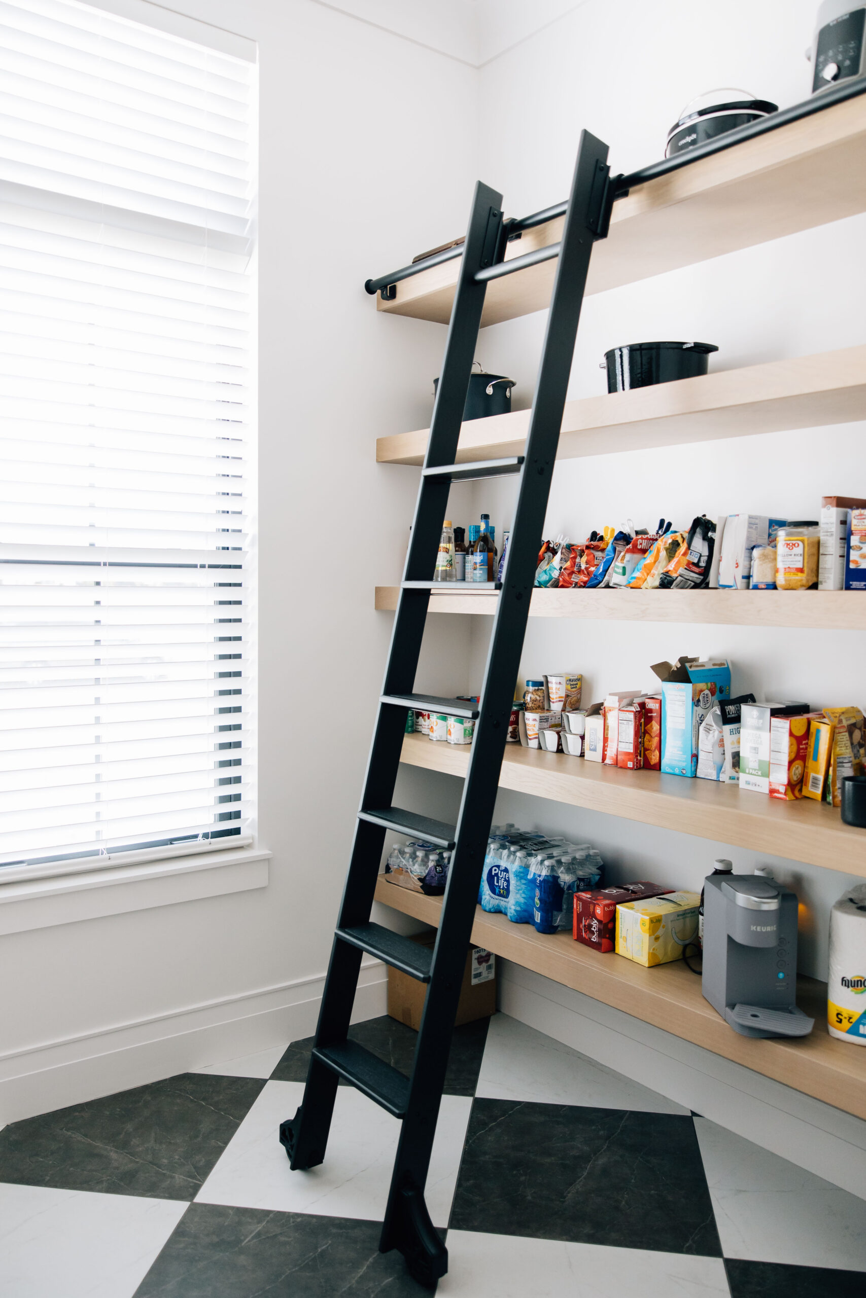 Walk-in pantry with floating wood shelves and black rolling ladder.