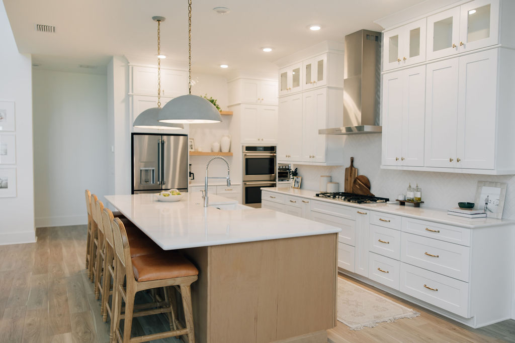 Transitional white kitchen with wood island and oversized pendants in a new construction home.