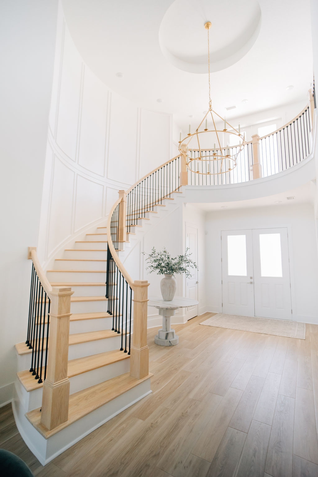 Bright entryway with curved staircase, chandelier, and natural wood flooring in a new construction home.