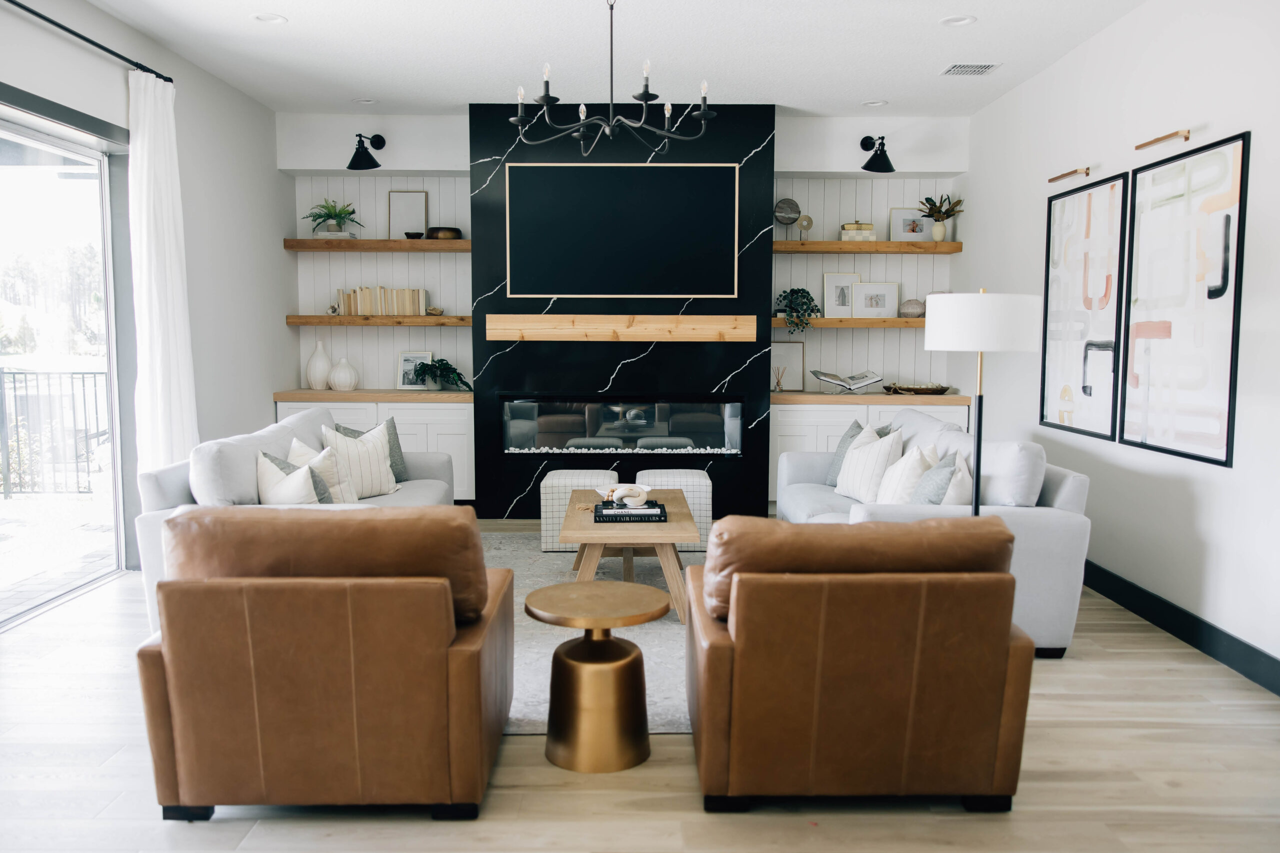 Living room with black feature fireplace, built-ins, leather chairs, and a modern chandelier.