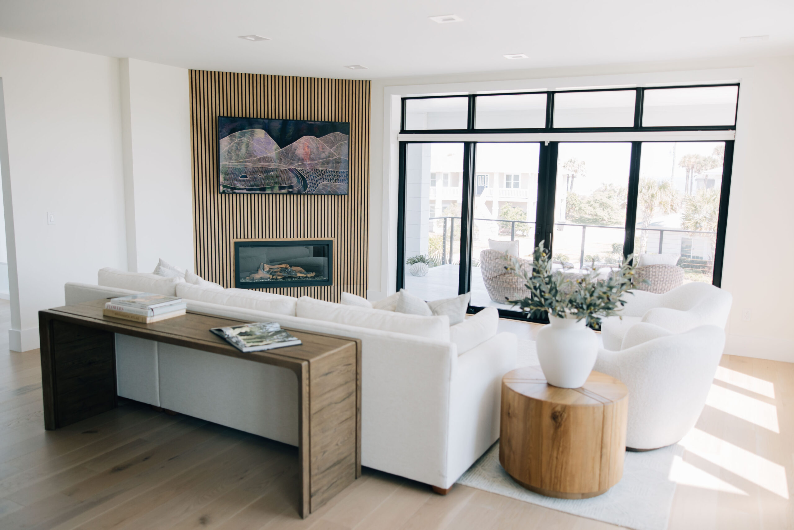 Beautifully renovated bright living room with custom feature wall, large windows, and white furniture.