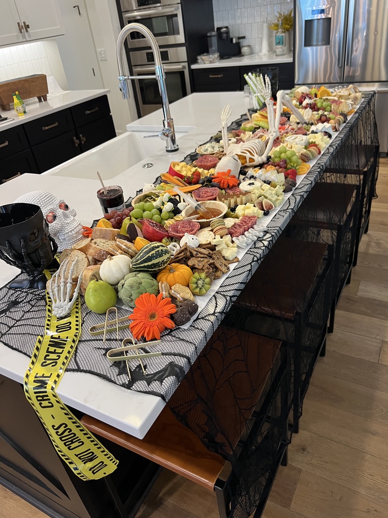 Large grazing board styled with skeletons, fruits, cheeses, and treats as a centerpiece for Halloween party entertaining.