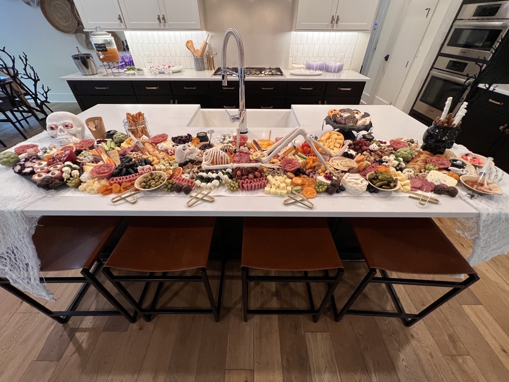Grazing board filled with cheeses, fruits, meats, and Halloween treats styled on a kitchen island for a Halloween party.
