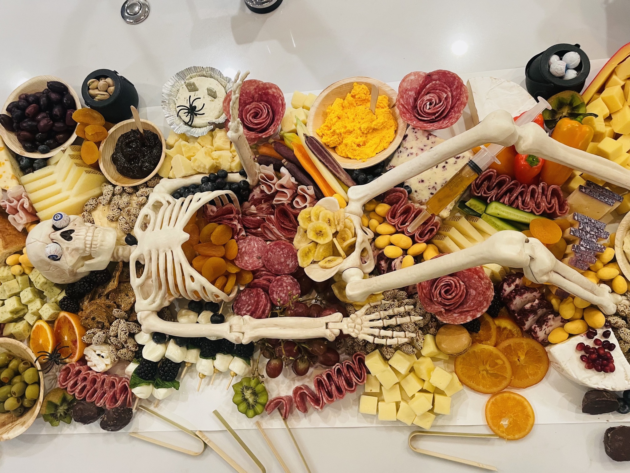 Skeleton prop arranged among charcuterie, fruit, and themed Halloween treats on a grazing board.