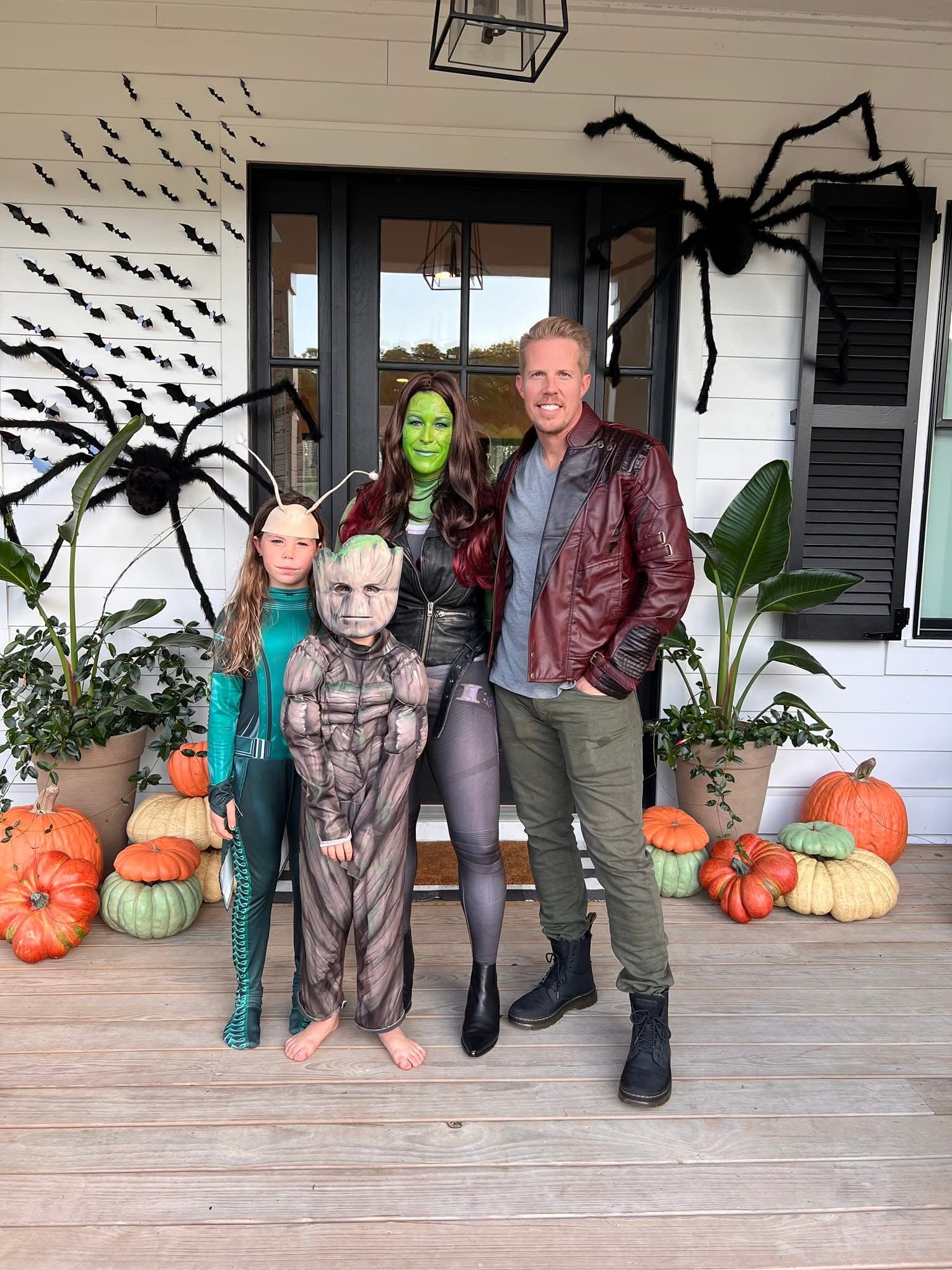 Family in Guardians of the Galaxy themed costumes posing on a front porch decorated with pumpkins, bats, and giant spiders as part of stylish Halloween party decor.