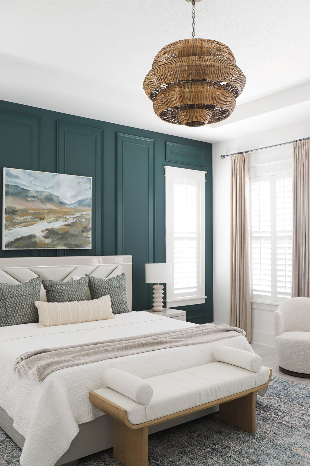 Sophisticated guest bedroom with teal green accent wall, rattan chandelier, and white bench seating.