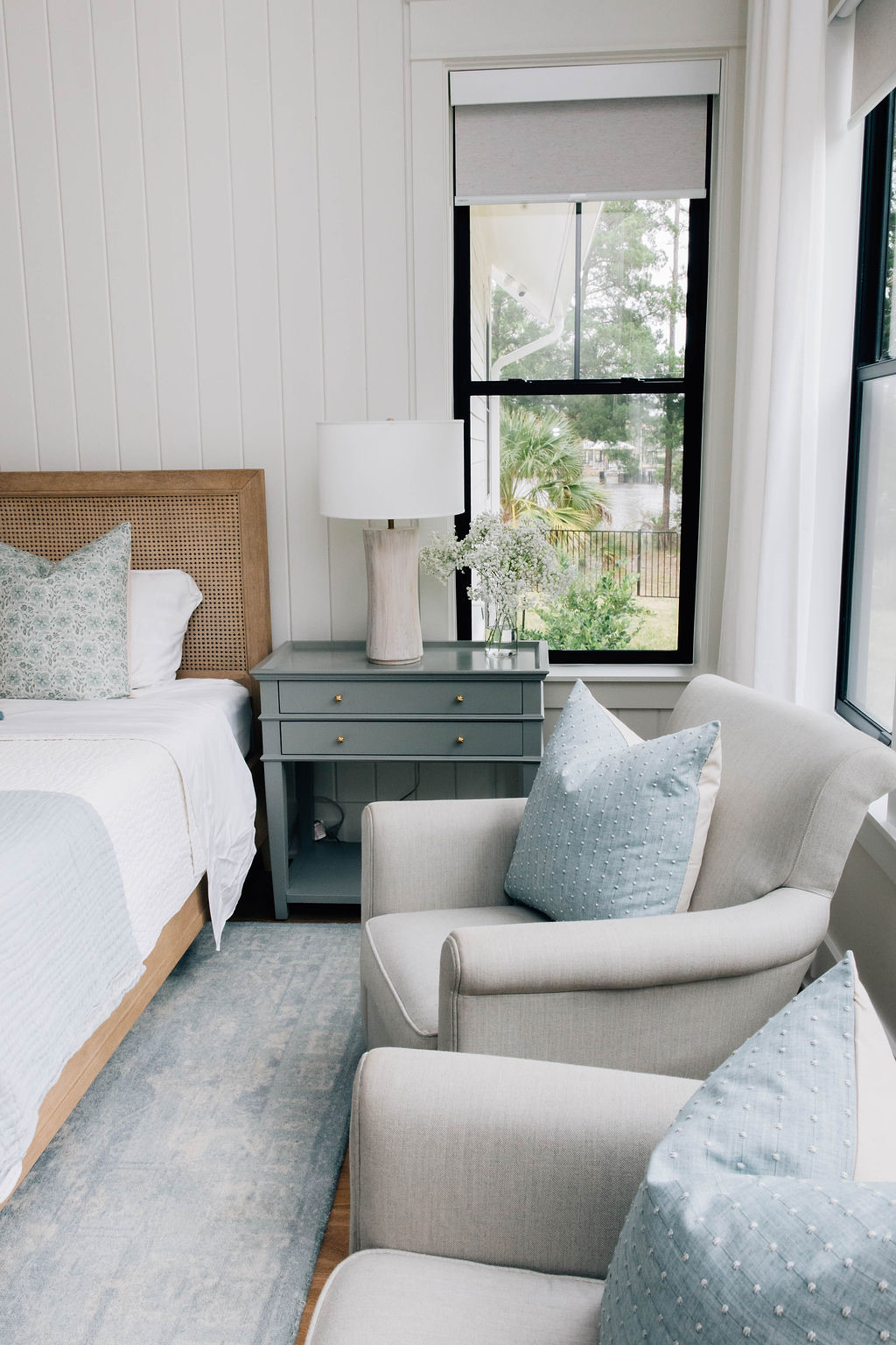 Blue and white guest bedroom with wood and cane headboard, soft blue accents, and cozy armchairs.
