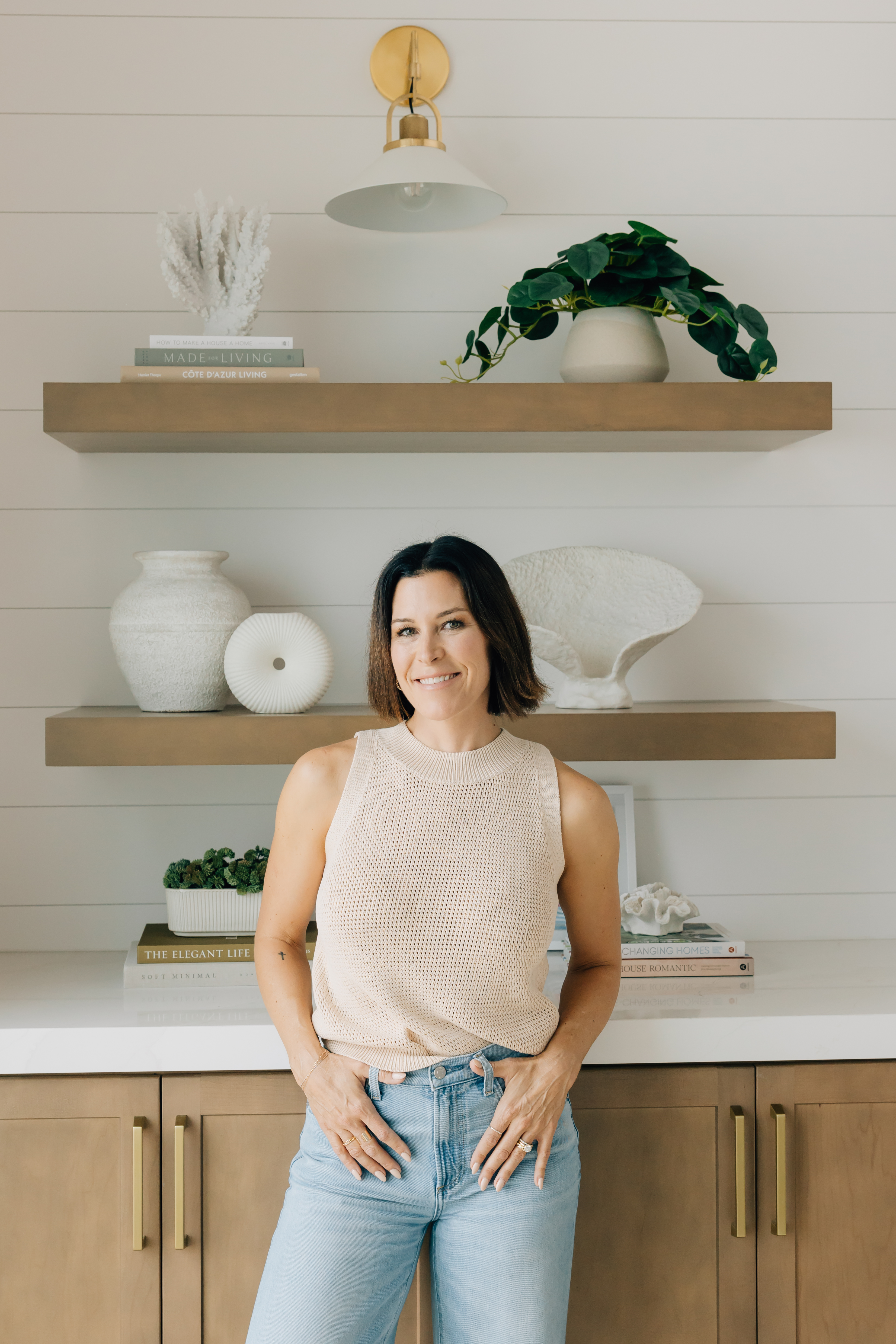Portrait of Jessica Woodward standing in front of built-in shelves and styled cabinetry in a modern coastal home.
