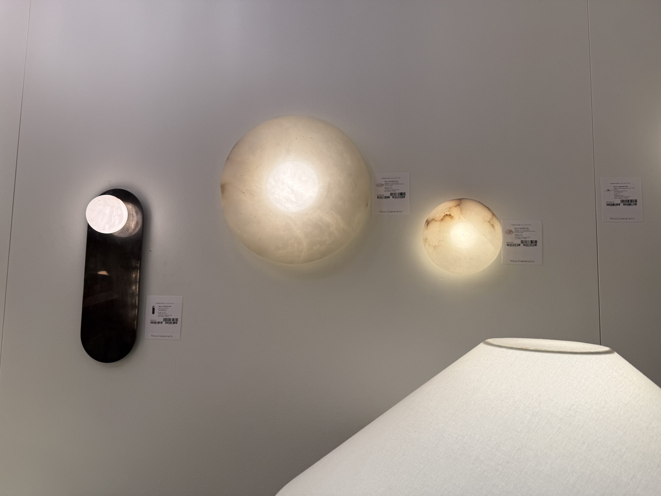 Three alabaster wall lights in various sizes glowing softly against a white wall.