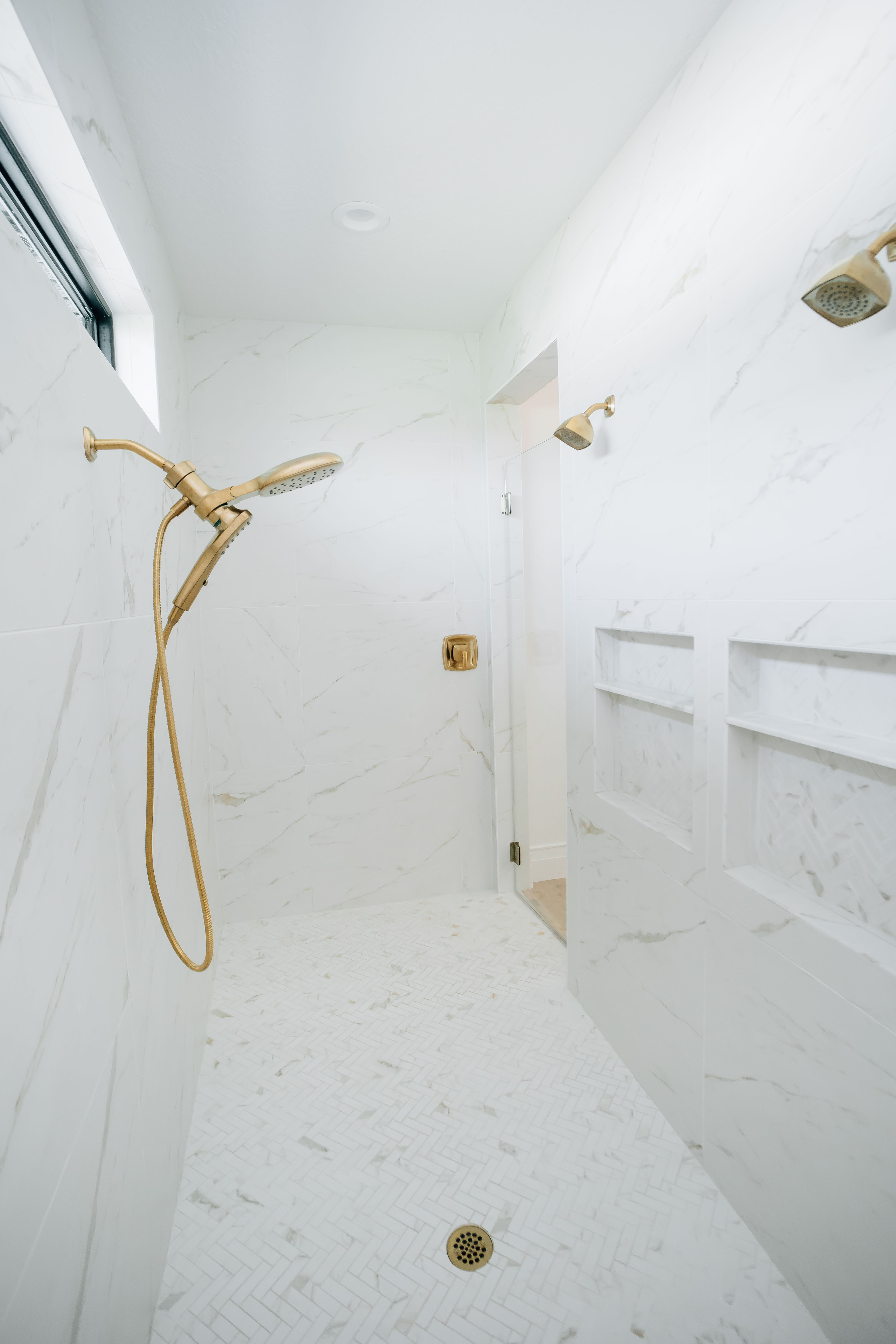 This gorgeous white marble shower features gold fixtures, two stationary shower heads, and one take-down shower head.