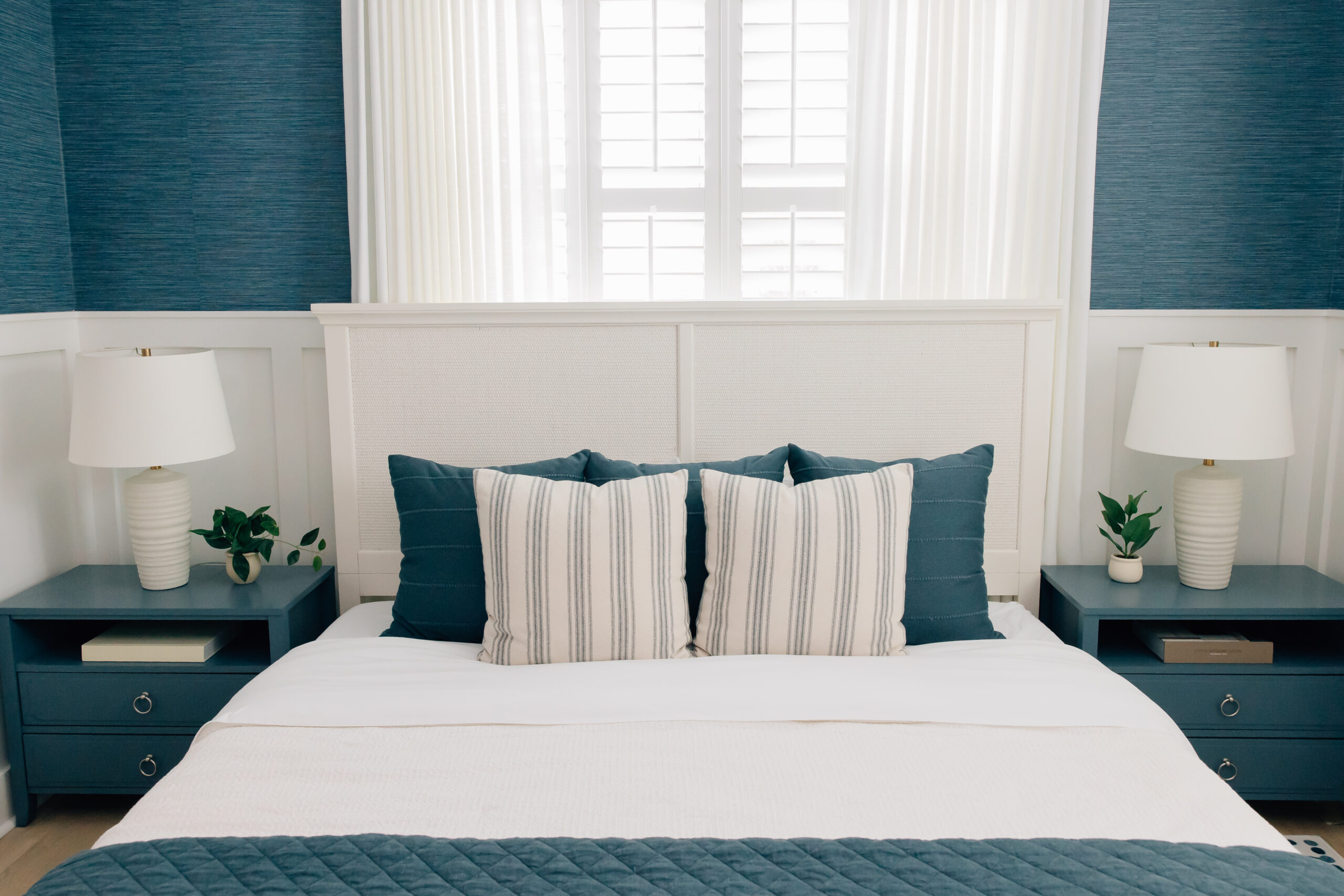 A cozy coastal bedroom with saturated blue, textured walls, matching nightstands, and layered linens.