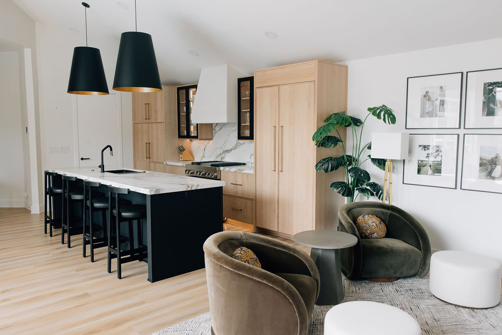 A custom home design kitchen with a marble and black island, black pendant lights, and natural wood cabinets.