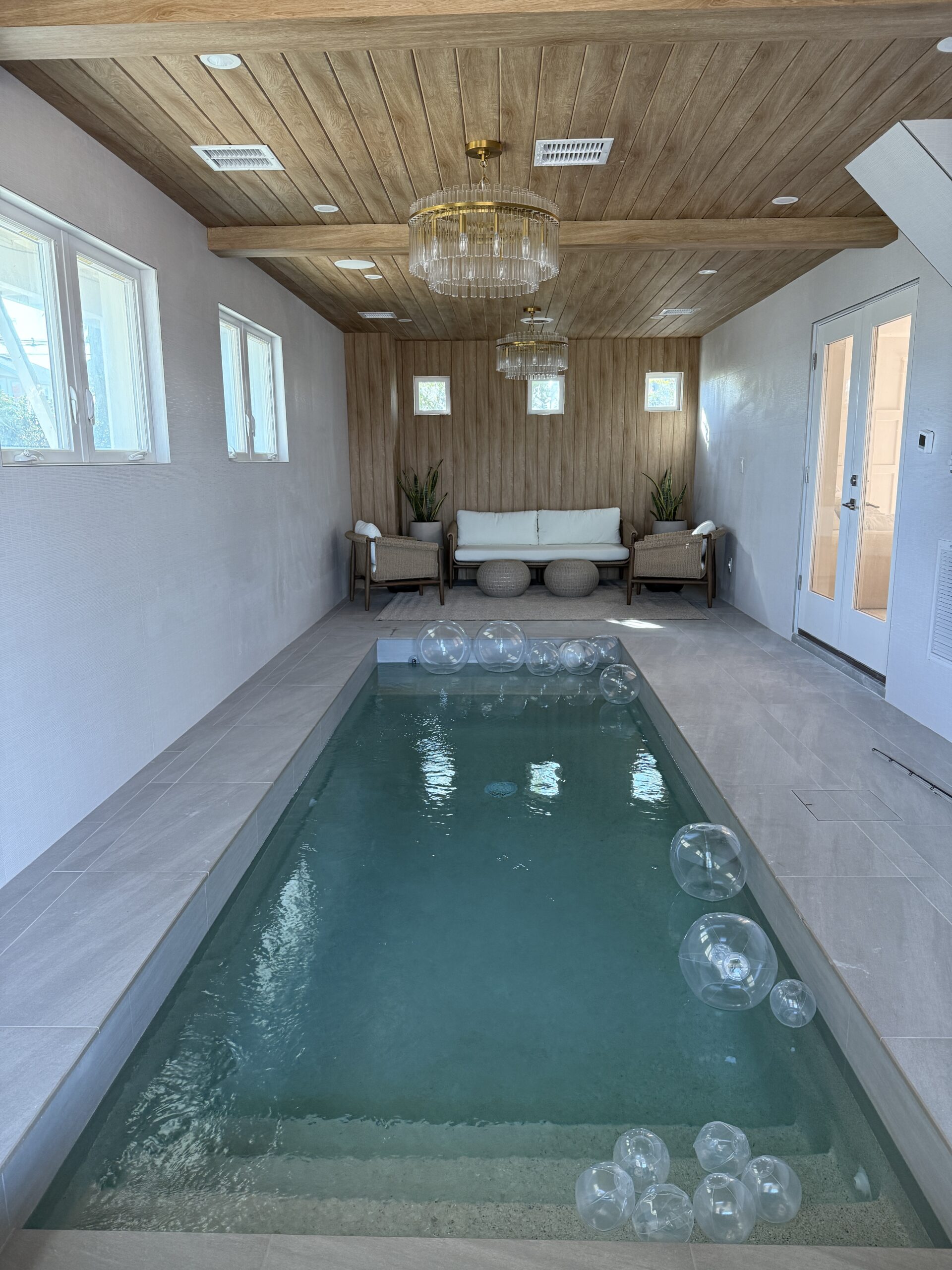 Indoor lap pool with wood ceiling and accent wall, comfortable sitting area, and cozy ambiance.