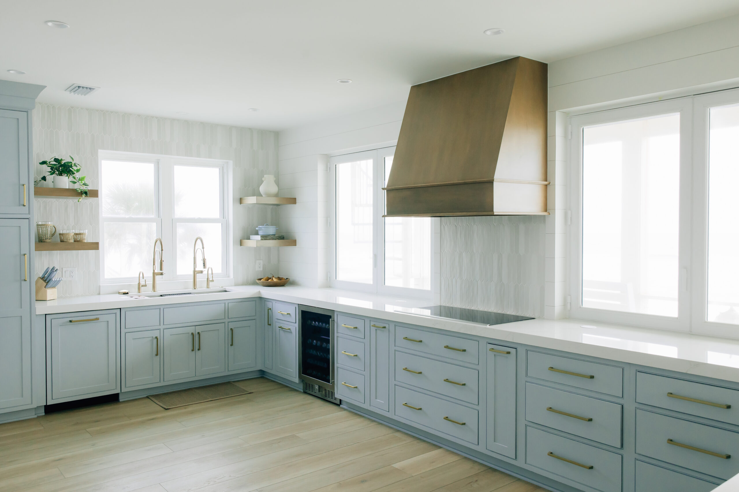 Large kitchen with textured, white walls, a custom gold range hood, and light coastal blue cabinets with gold hardware.

