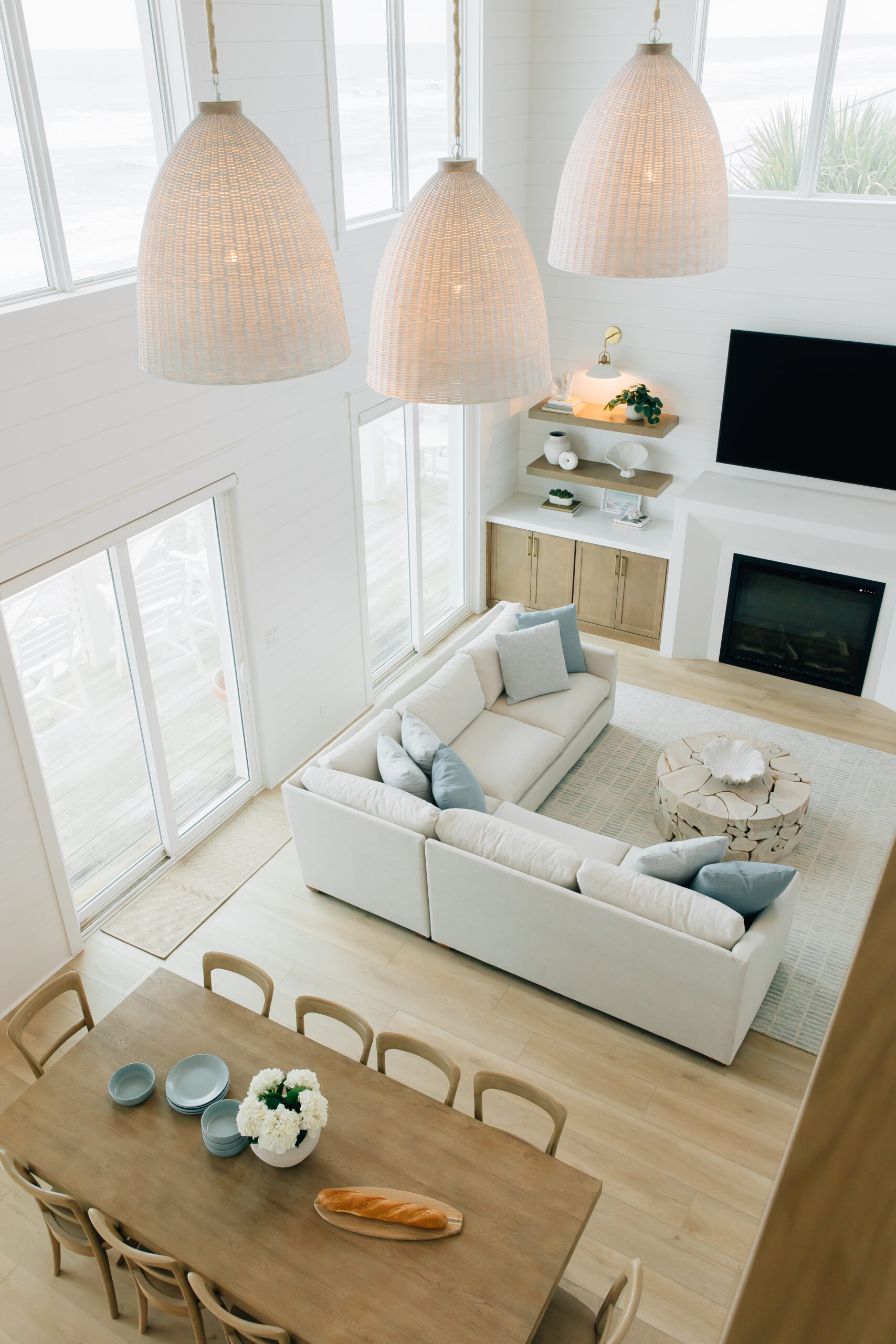 Overhead shot of a living and dining room with lots of natural wood color, a white sofa, textured lighting, and coastal blue decor accents.
