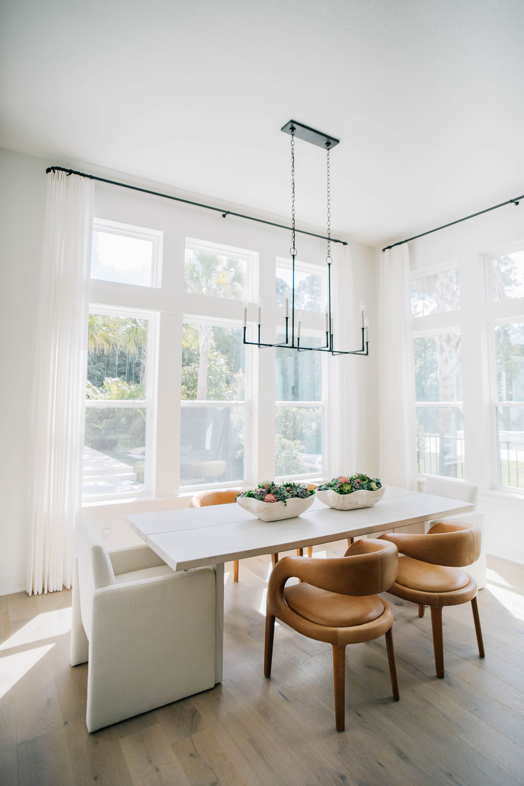 Bright dining room in a Ponte Vedra Beach home with non-matching dining chairs, warm brown leather seating, white upholstered end chairs, and large windows reflecting current interior design trends.