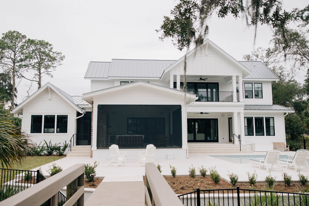Large white Florida home with a covered lanai, screened outdoor living area, pool deck, and lounge chairs overlooking the backyard.