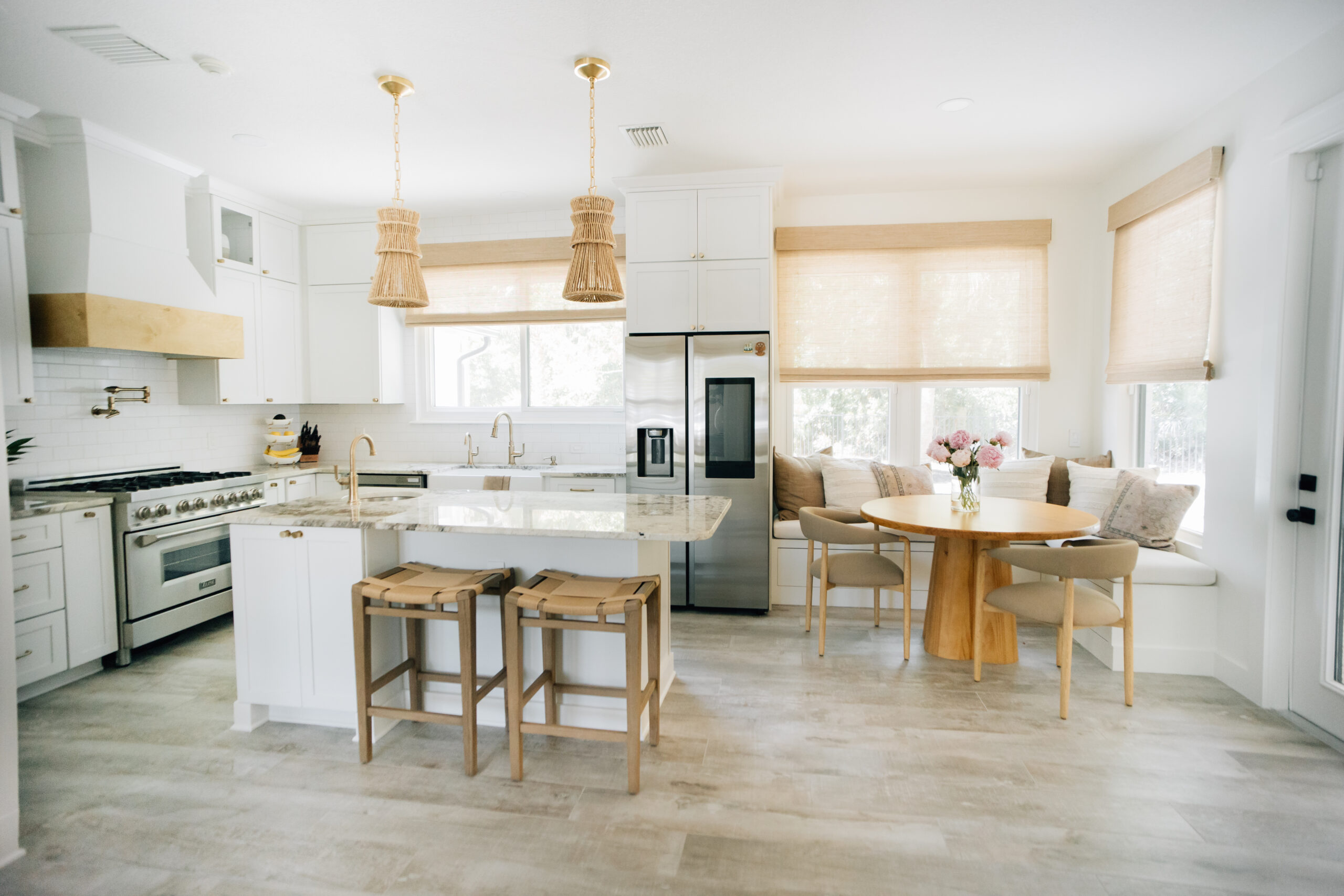 A bright white kitchen featuring a large island, woven pendant lights, built-in breakfast nook seating, natural wood accents, and ample storage cabinetry.