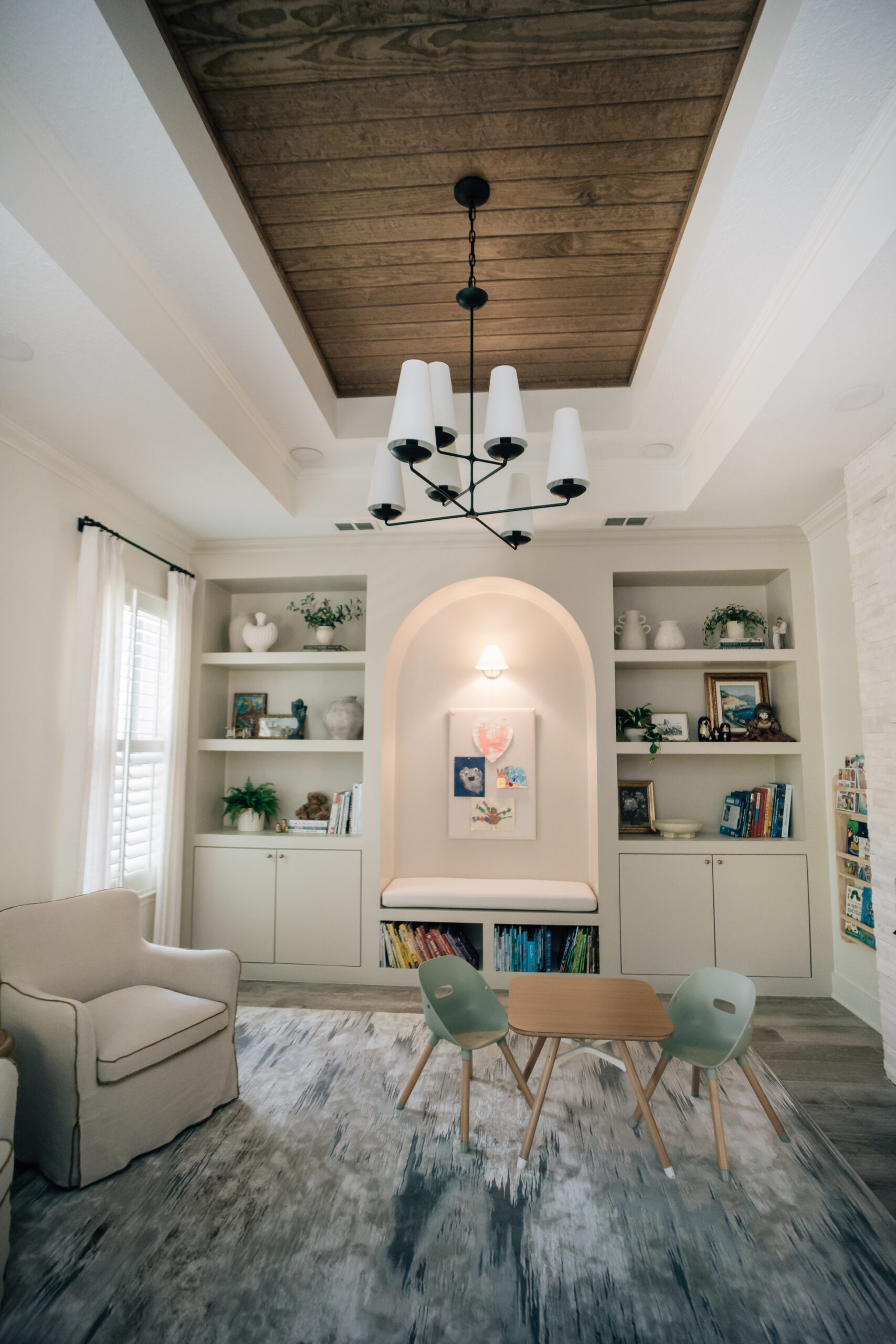 A bright family living room with custom built-in shelving, concealed storage cabinets, a reading nook, children's books, and a small activity table.