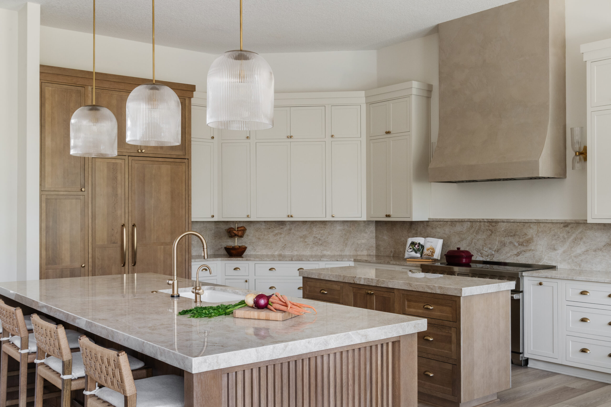 Luxury kitchen with a large waterfall island, custom white and wood cabinetry, oversized range hood, pendant lighting, and extensive built-in storage.