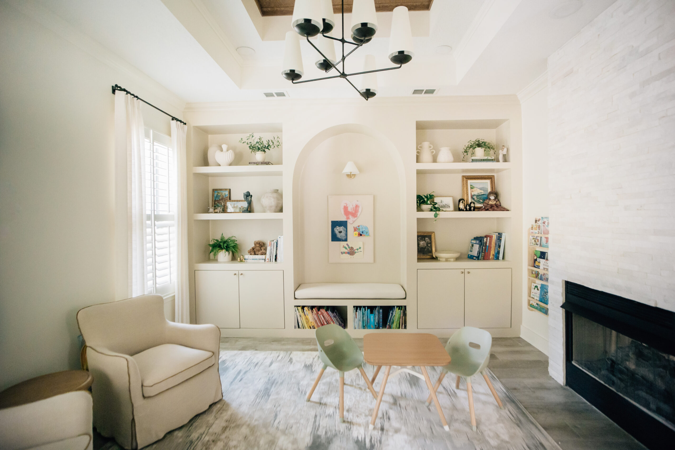 Custom children's playroom in a new construction home with built-in shelving, reading nook, fireplace, soft neutral furnishings, and organized toy storage.