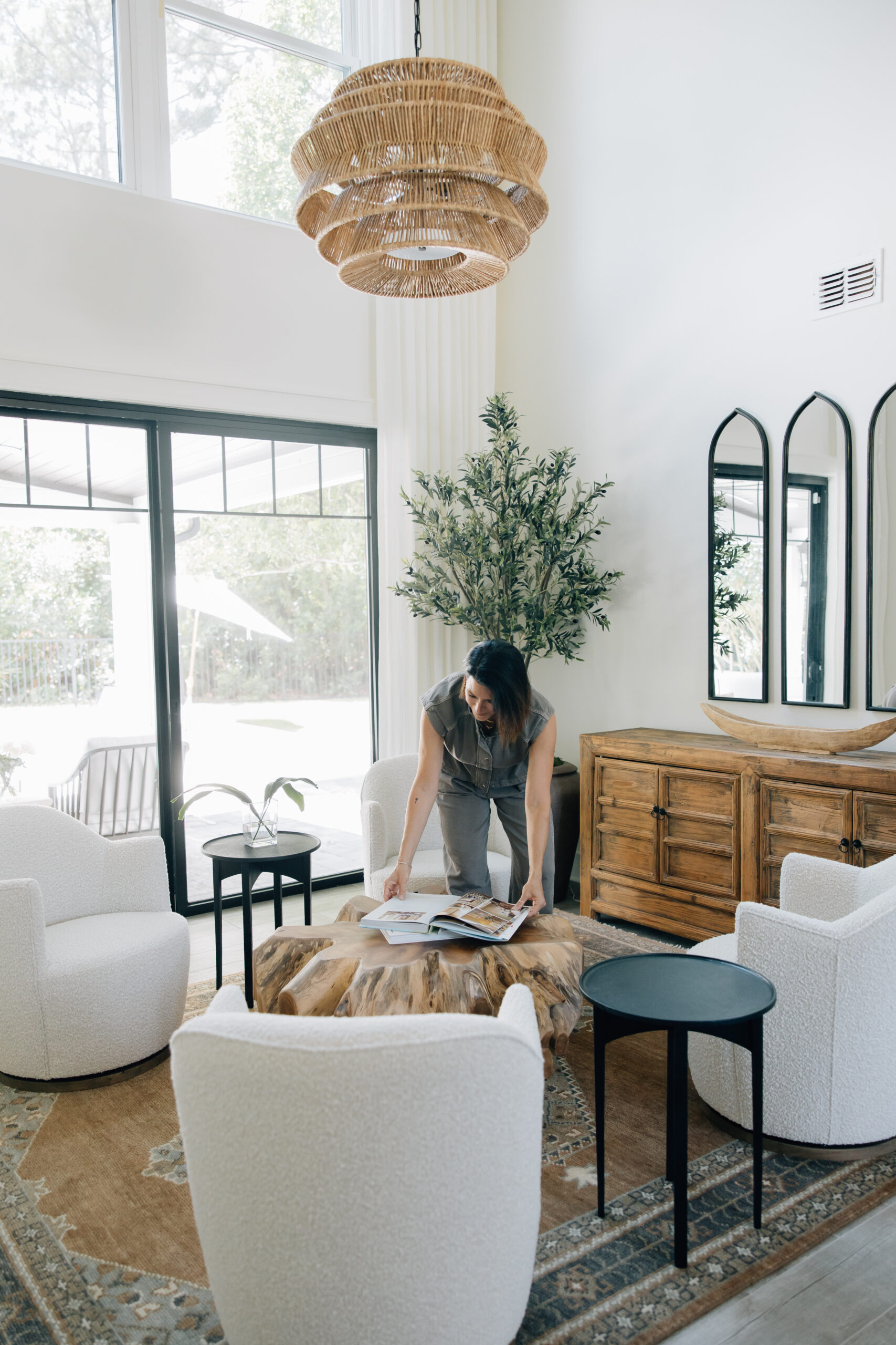 Bright living room in a new construction home with soaring ceilings, oversized windows, boucle chairs, natural wood furniture, and a woven statement chandelier.