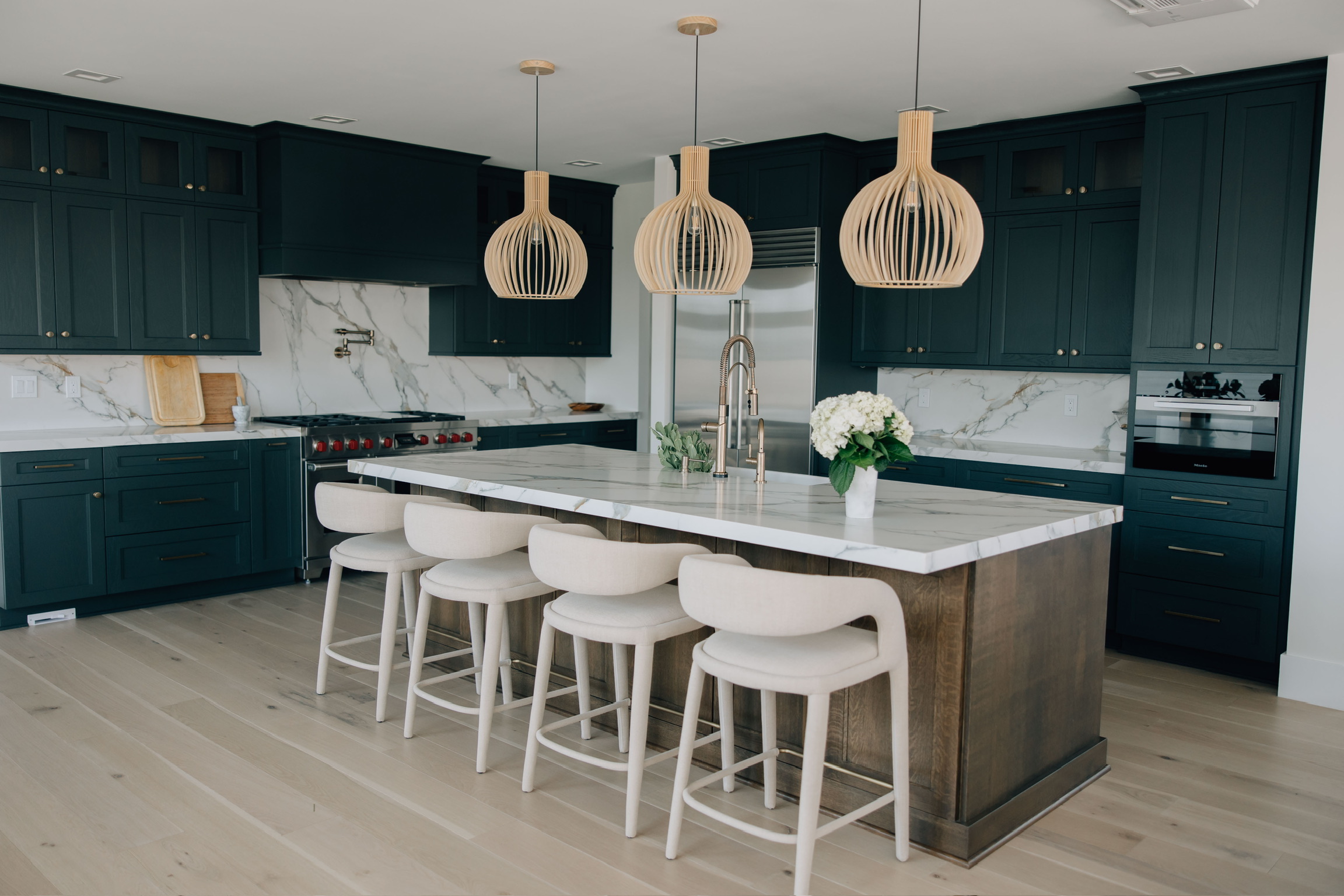 Spacious kitchen with dark cabinetry, quartz countertops, wood pendant lights, and a large island with four upholstered stools.